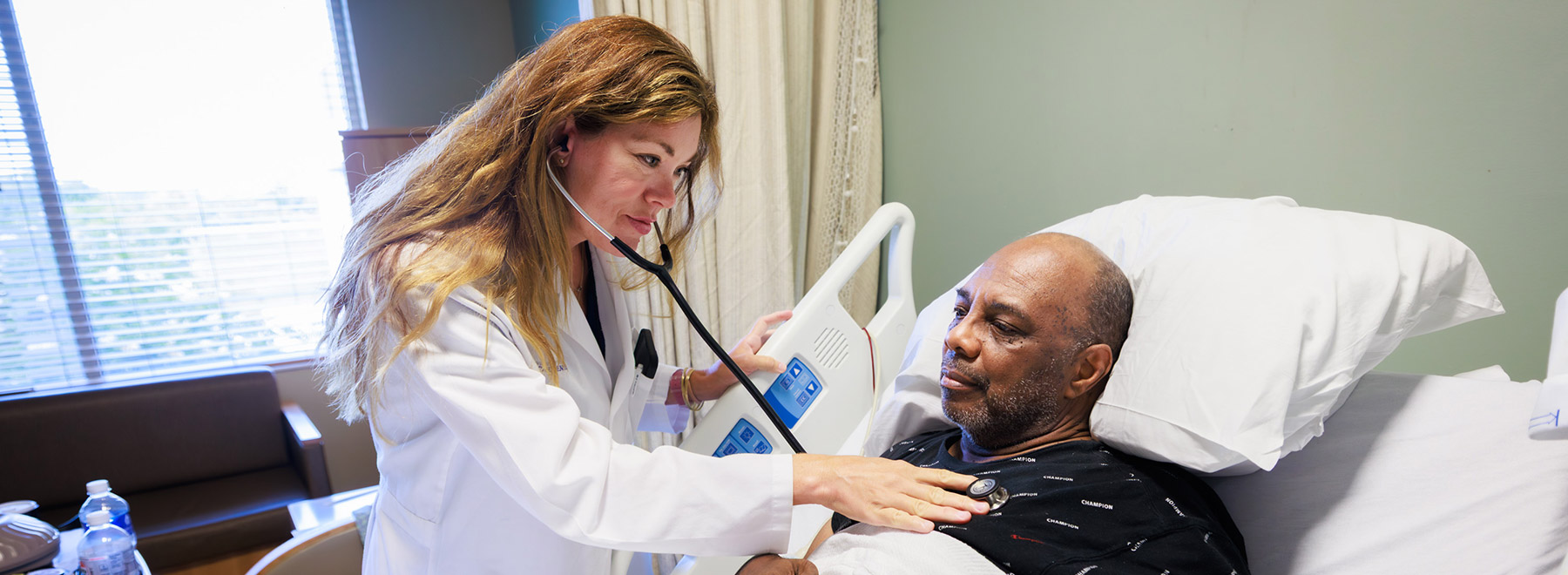 Dr. Laura Fincher, hospitalist and assistant professor of medicine, uses stethoscope to listen to patient Ronnie Green's heart and lungs.